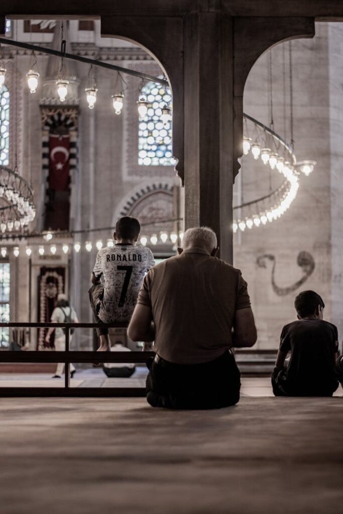 Three people of different ages seated inside a beautifully lit historic mosque, emphasizing tranquility and spirituality.